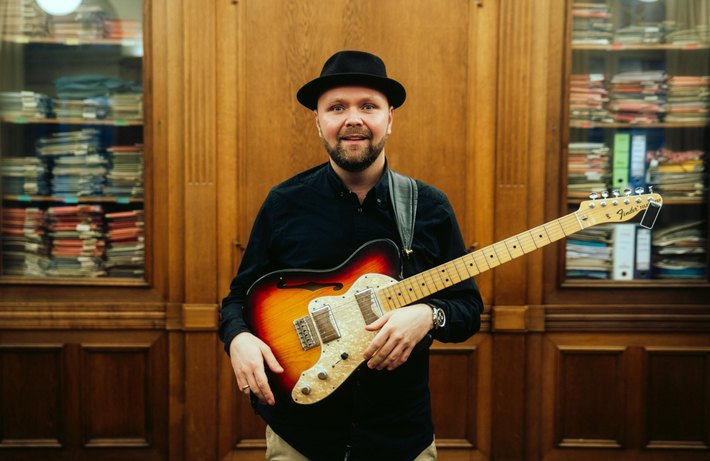 Marcus Armani mit Gitarre vor einem Plattenschrank
